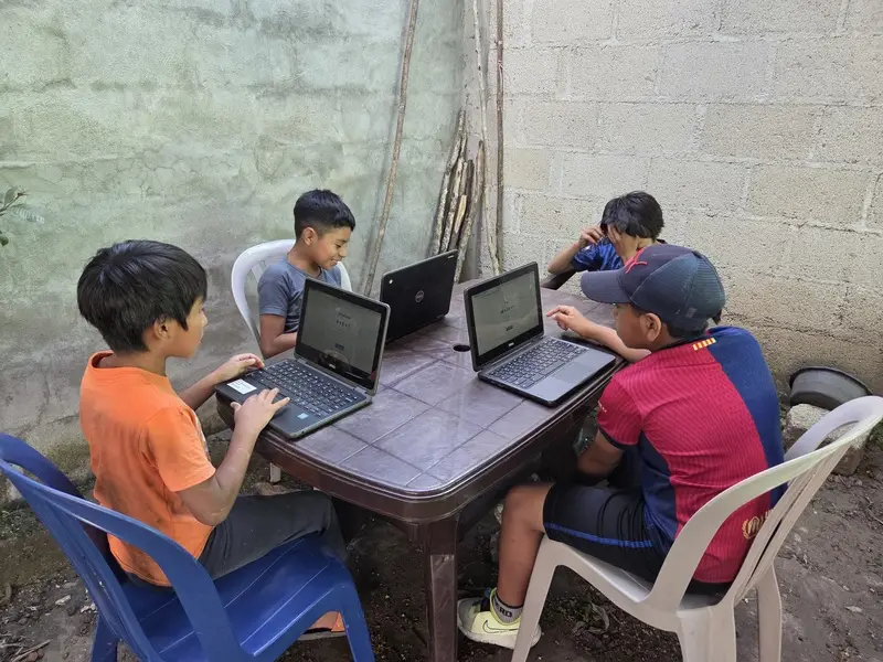 Niños trabajando en una mesa con laptops